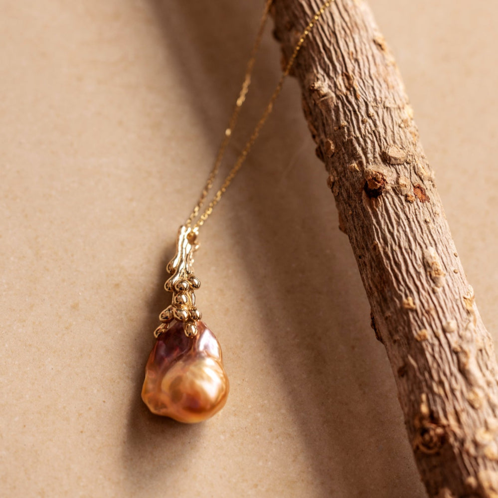 An organic Baroque Pearl necklace draped over a branch on a beige background