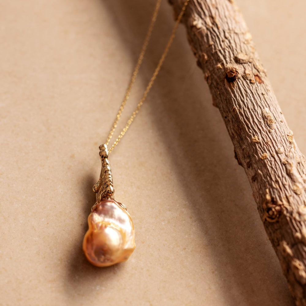 An organic Baroque Pearl necklace draped over a branch on a beige background