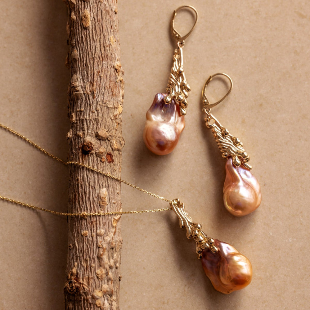 Pair of organic Baroque pearl earrings and a pendant with gold bail and clasps on a beige background.