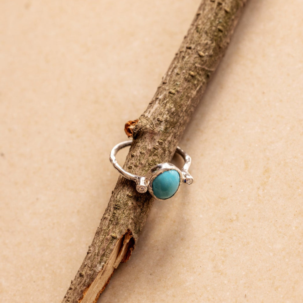 Organic Silver ring with a turquoise and two diamonds on a wooden branch against a beige background