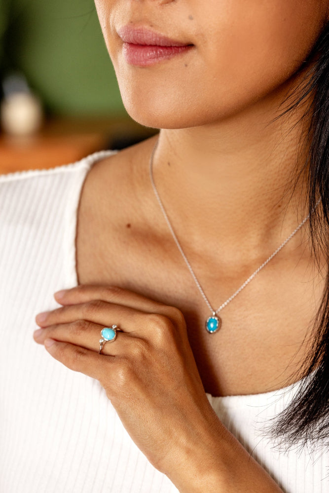 Close-up of a person wearing a silver turquoise pendant and ring.