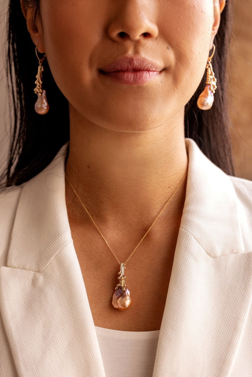 Close-up of a person wearing a gold necklace with an organic Baroque pearl pendant and matching earrings.