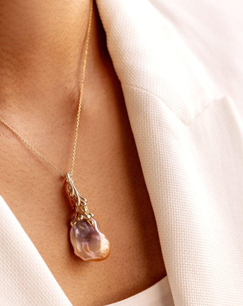 Gold necklace with a Baroque Pearl pendant worn by a person against a neutral background