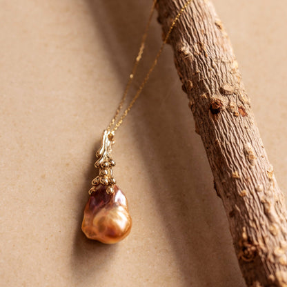 An organic Baroque Pearl necklace draped over a branch on a beige background