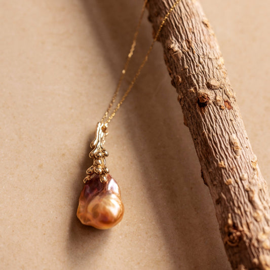 An organic Baroque Pearl necklace draped over a branch on a beige background