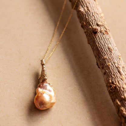 An organic Baroque Pearl necklace draped over a branch on a beige background