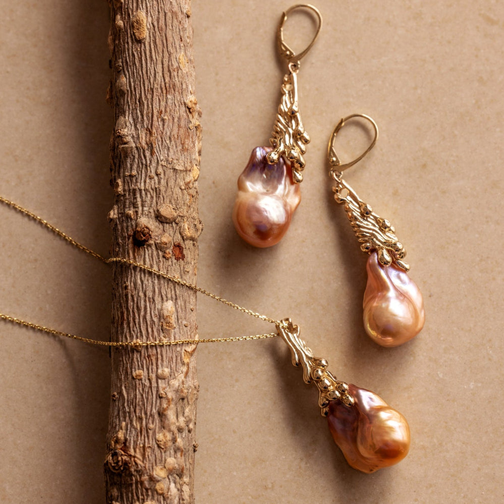 Pair of organic Baroque pearl earrings and a pendant with gold bail and clasps on a beige background.