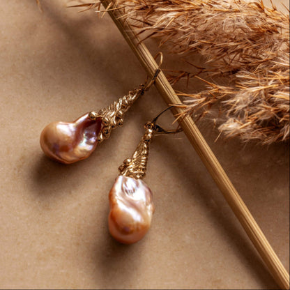 Pair of pearl earrings on a beige background with dried grasses.