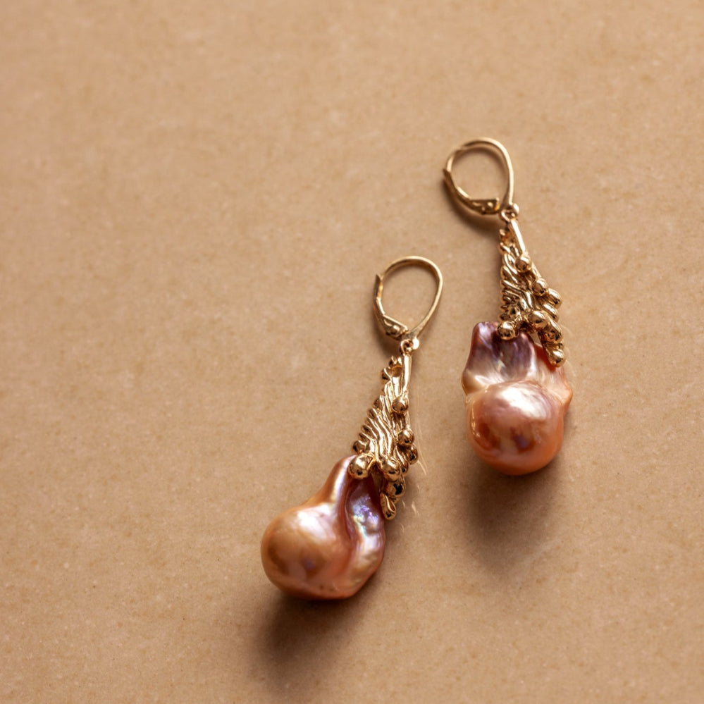 Pair of organic Baroque pearl earrings with gold clasps on a beige background