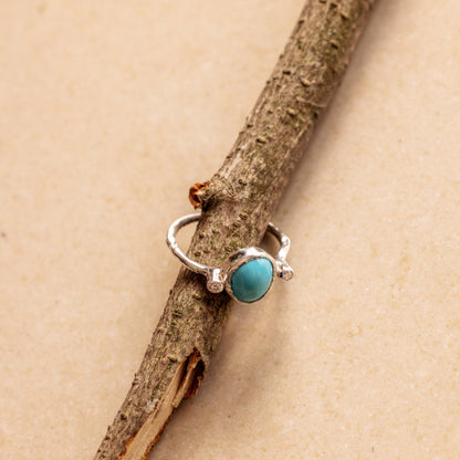 Organic Silver ring with a turquoise and two diamonds on a wooden branch against a beige background