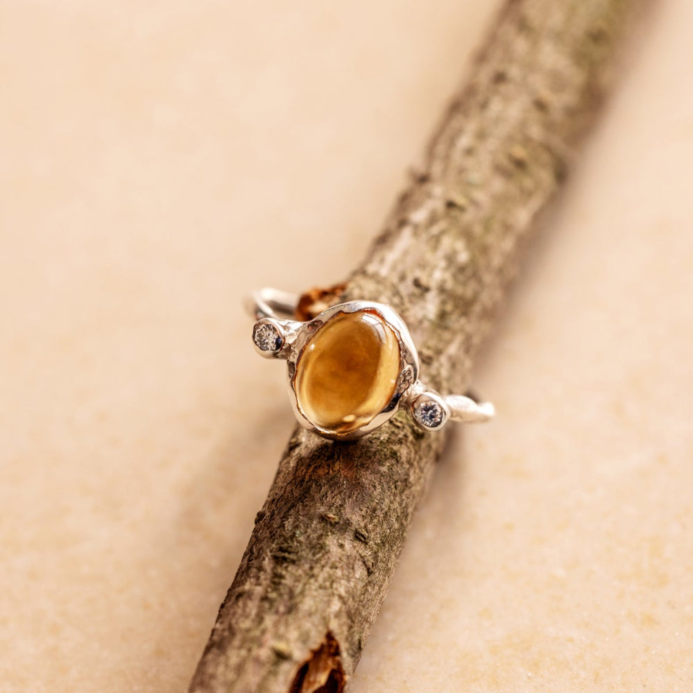 An organic style silver ring with a yellow citrine and two little diamonds on either side of the gemstone on a tree branch.