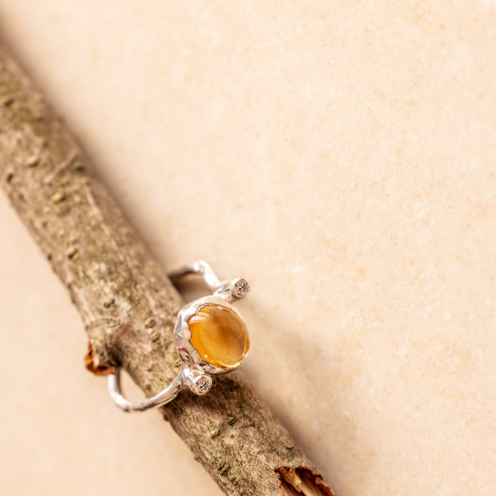 An organic style silver ring with a yellow citrine and two little diamonds on either side of the gemstone on a tree branch.