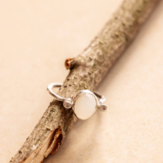 Organic style Silver ring with a moonstone and diamonds on either sides of it on a wooden branch