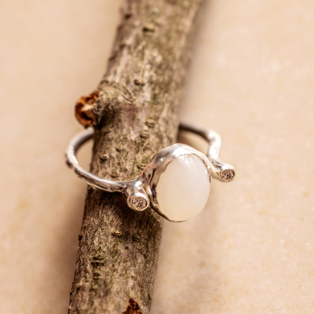 Organic style Silver ring with a moonstone and diamonds on either sides of it on a wooden branch