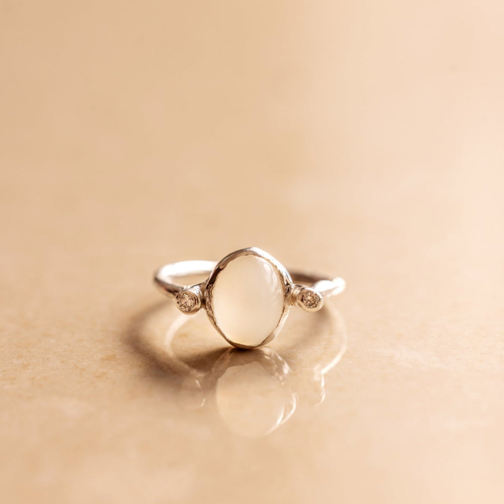 Organic style Silver ring with a moonstone and diamonds on either sides of it on a beige background.