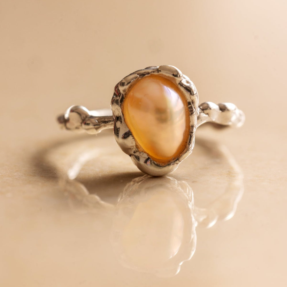 Silver ring with an organic pearl on a beige background