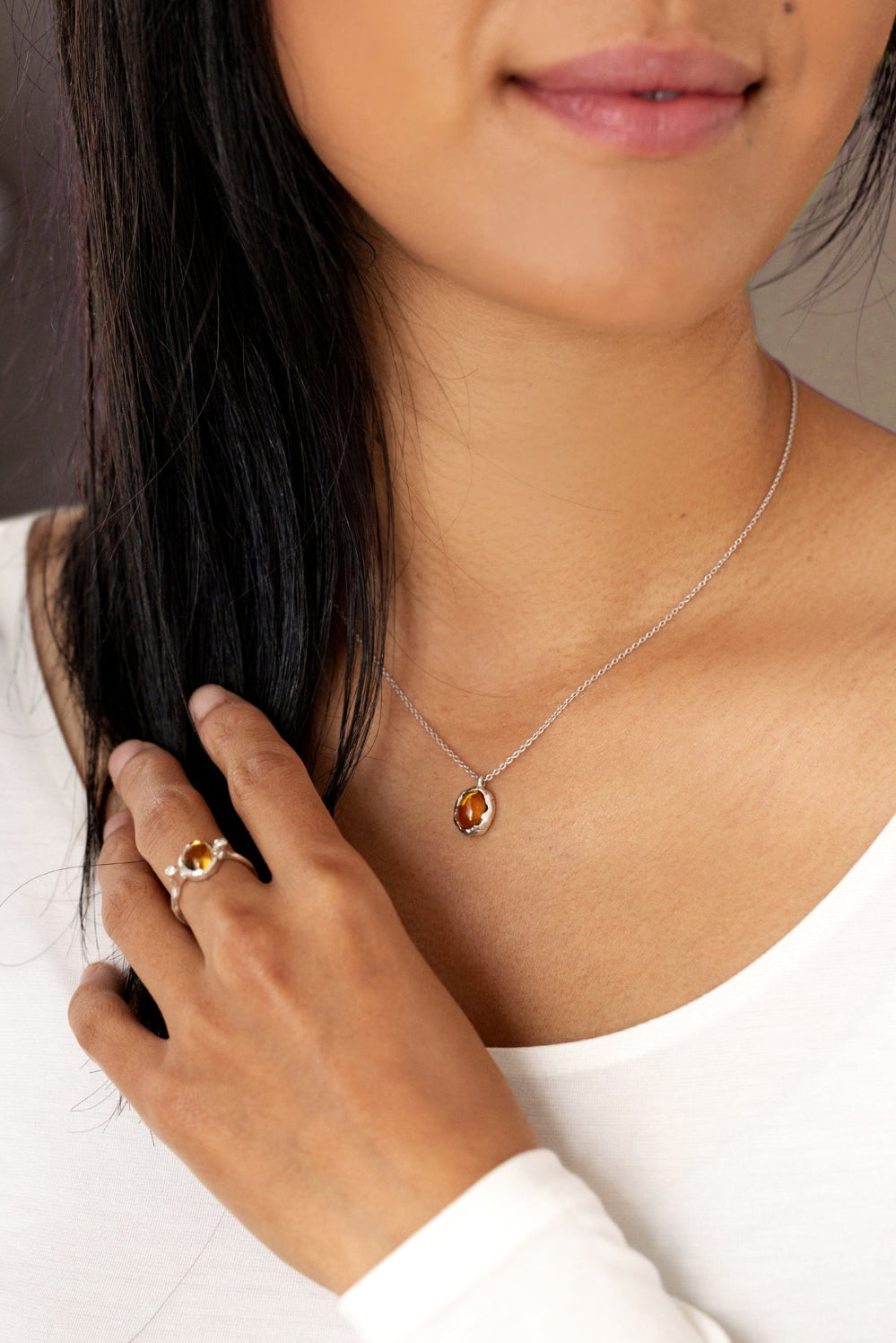 A woman wearing a silver ring and necklace, featuring an organic-style silver ring and a yellow citrine gemstone.