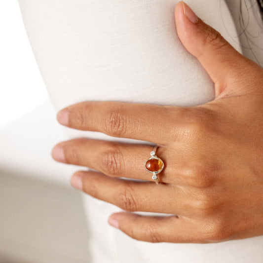 Hand wearing an organic style silver ring with a yellow citrine and two little diamonds on either side of the gemstone on a white background.