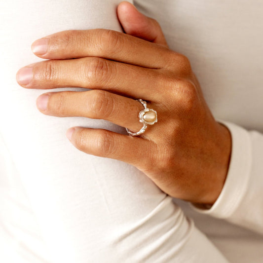 A hand wearing an organic pearl ring, holding a white cushion.