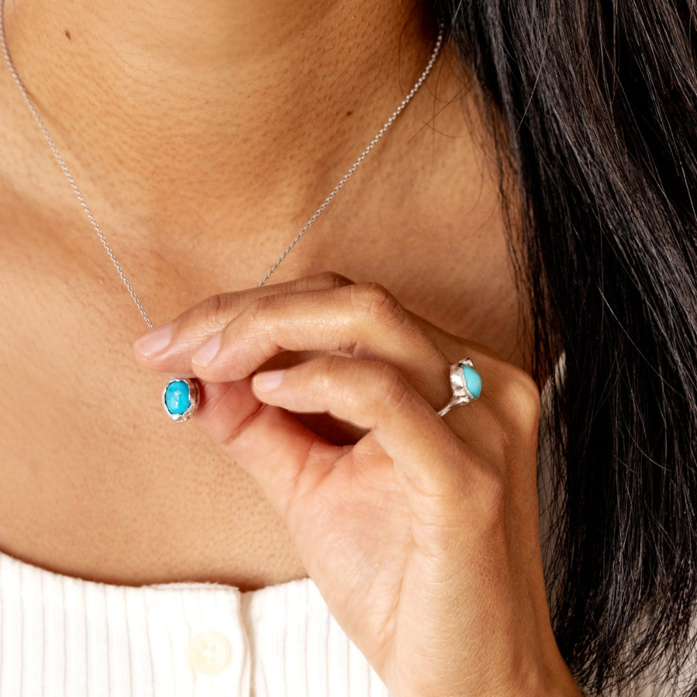 Close-up of a person wearing a turquoise pendant necklace and ring.