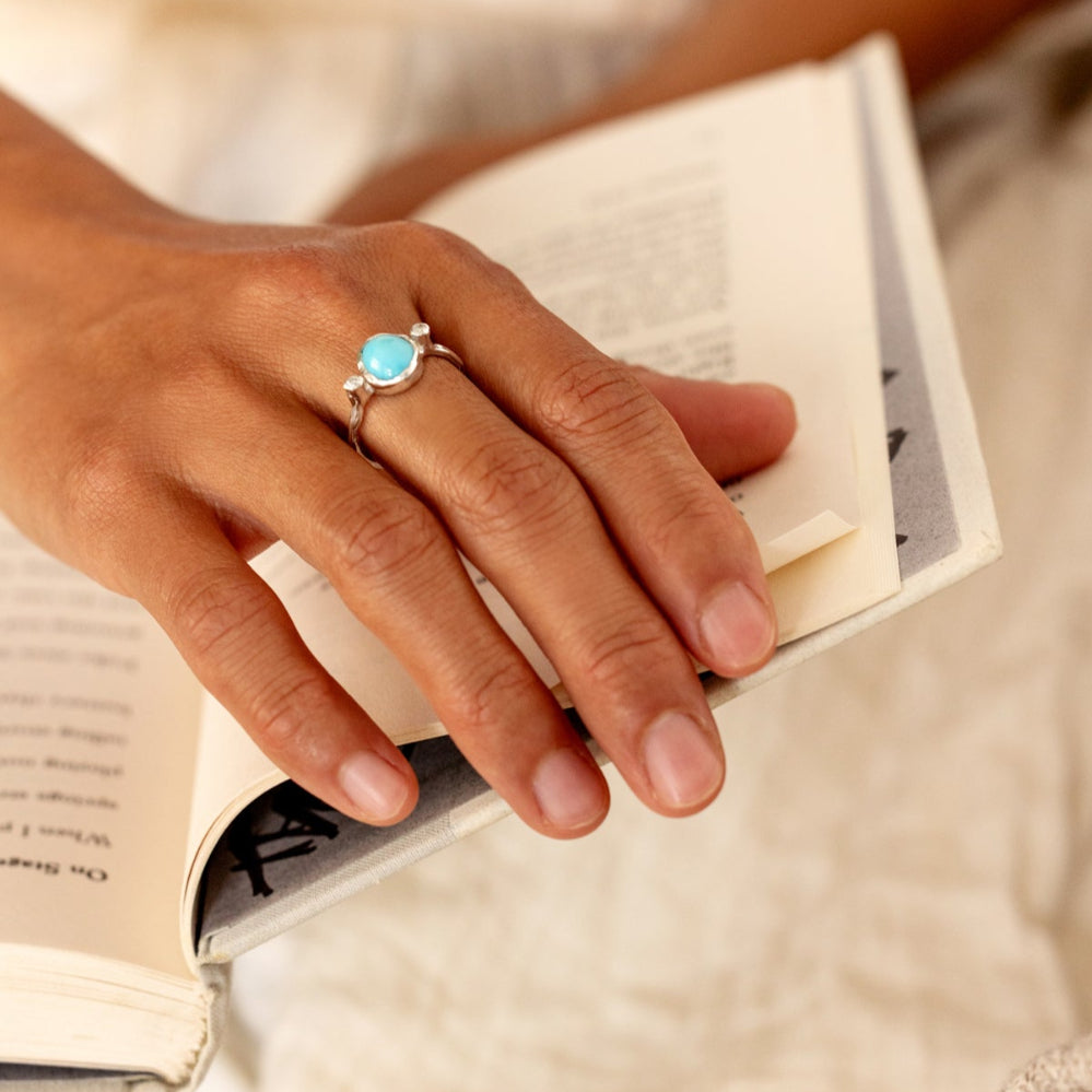 A hand wearing a turquoise ring on an open book