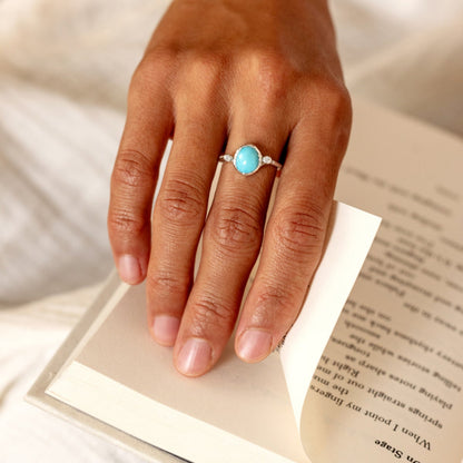 Hand wearing a ring with a turquoise stone on an open book