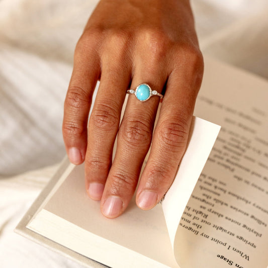 Hand wearing a ring with a turquoise stone on an open book