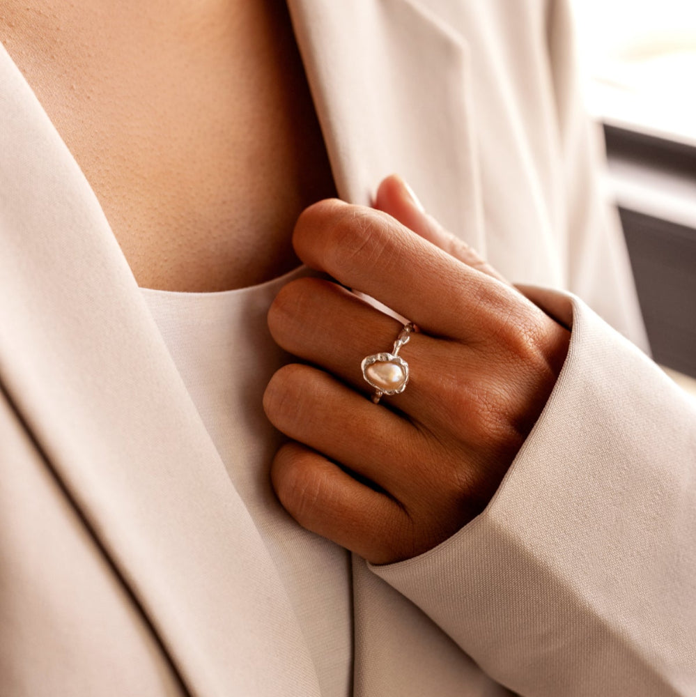 Close-up of a hand wearing an organic-shaped pearl silver ring holding a beige garment.