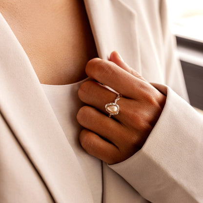 Close-up of a hand wearing an organic-shaped pearl silver ring holding a beige garment.