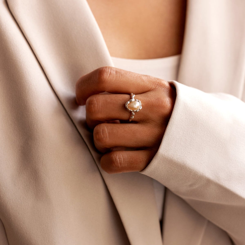 Close-up of a hand wearing a pearl ring with a white blazer.