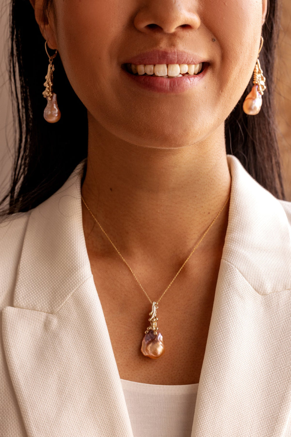 Woman wearing an organic Baroque pearl necklace and earrings with a neutral background.