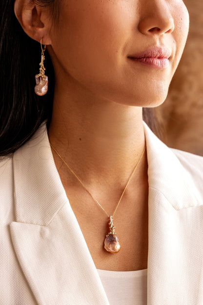 Close-up of a person wearing a gold necklace with an organic Baroque pearl pendant and matching earrings.