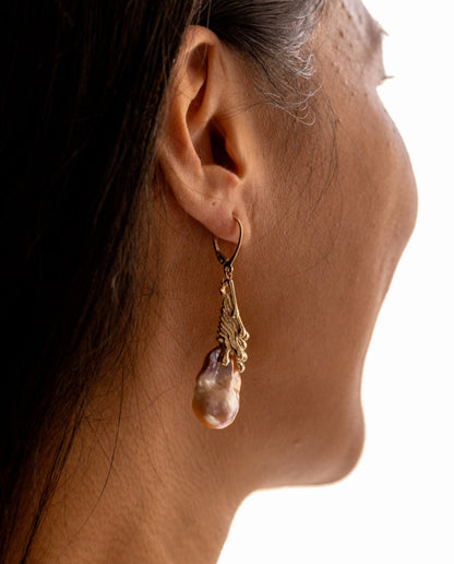 Close-up of a person wearing a gold earring with a pink organic baroque pearl pendant.