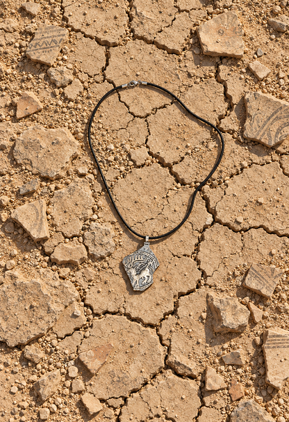 Handmade ancient Iranian inspired sterling silver stag pendant from the Shards Collection by Rooz Jewellery, with a stag with large antlers and a small figure in relief, dotted border and broken edge, on a black genuine leather cord