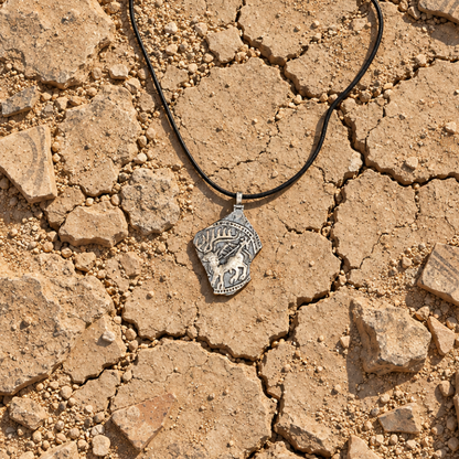 Handmade ancient Iranian inspired sterling silver stag pendant from the Shards Collection by Rooz Jewellery, with a stag with large antlers and a small figure in relief, dotted border and broken edge, on a black genuine leather cord