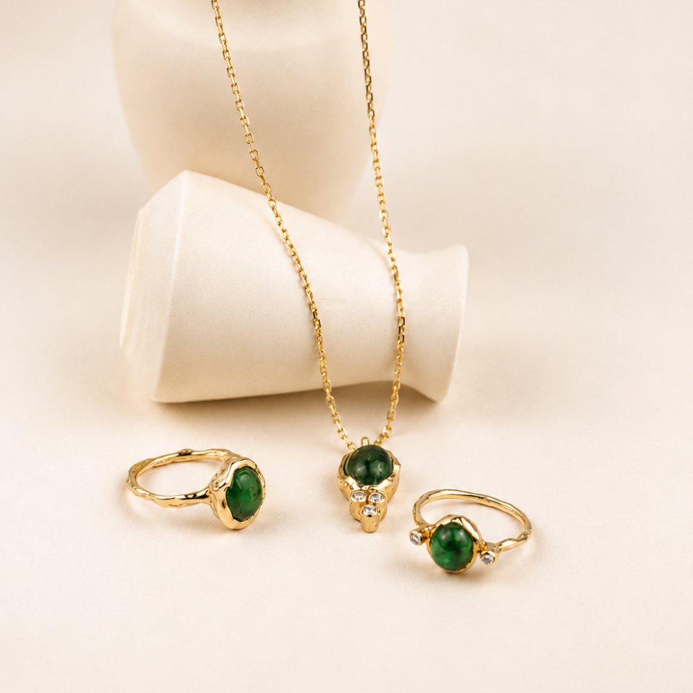 Handmade organic 10k yellow gold ring with a single green emerald oval cabochon, beside an emerald gold pendant with three diamonds and an emerlad gold ring with two diamonds, Rooz Jewellery Toronto